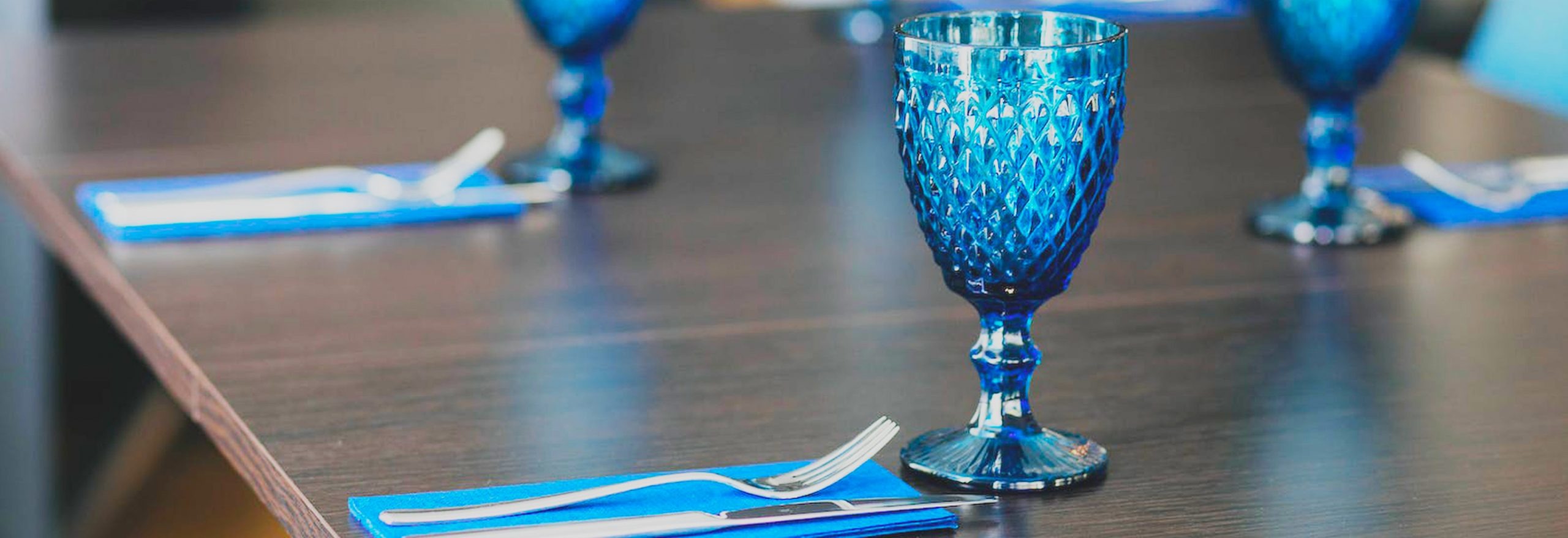 Tavola apparecchiata con calice blu e fazzoletti blu e forchetta